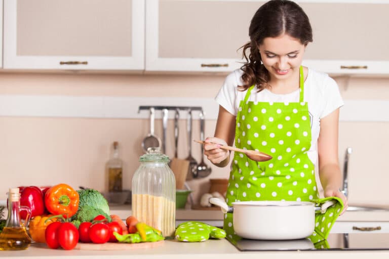A woman in a green apron is preparing food in a kitchen.