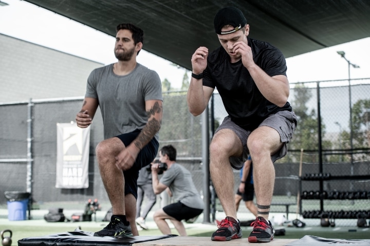 Two men squatting on a bench in a gym.