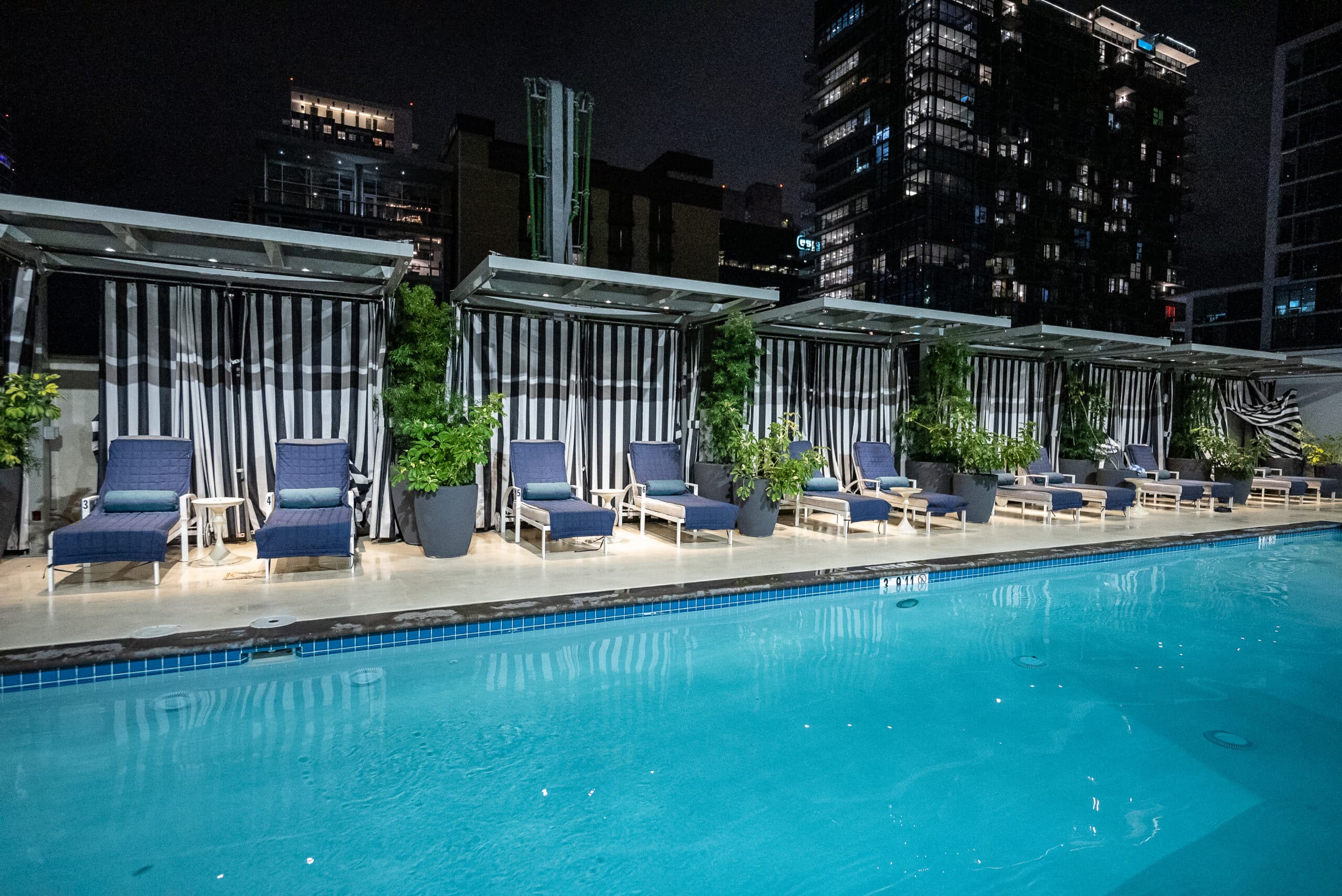 A swimming pool with lounge chairs and a skyscraper in the background.