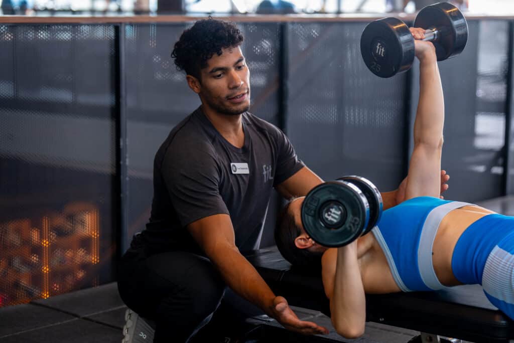 A man and a woman doing dumbbells in a gym.