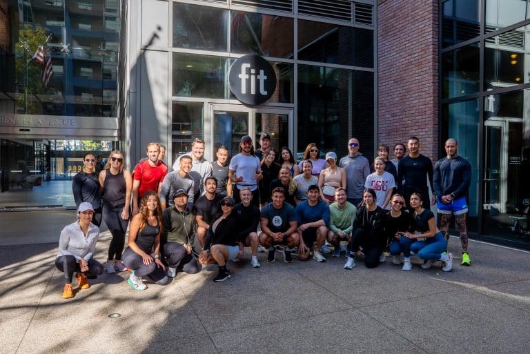 A group of people in athletic wear pose for a photo in front of a building with a "fit" sign.